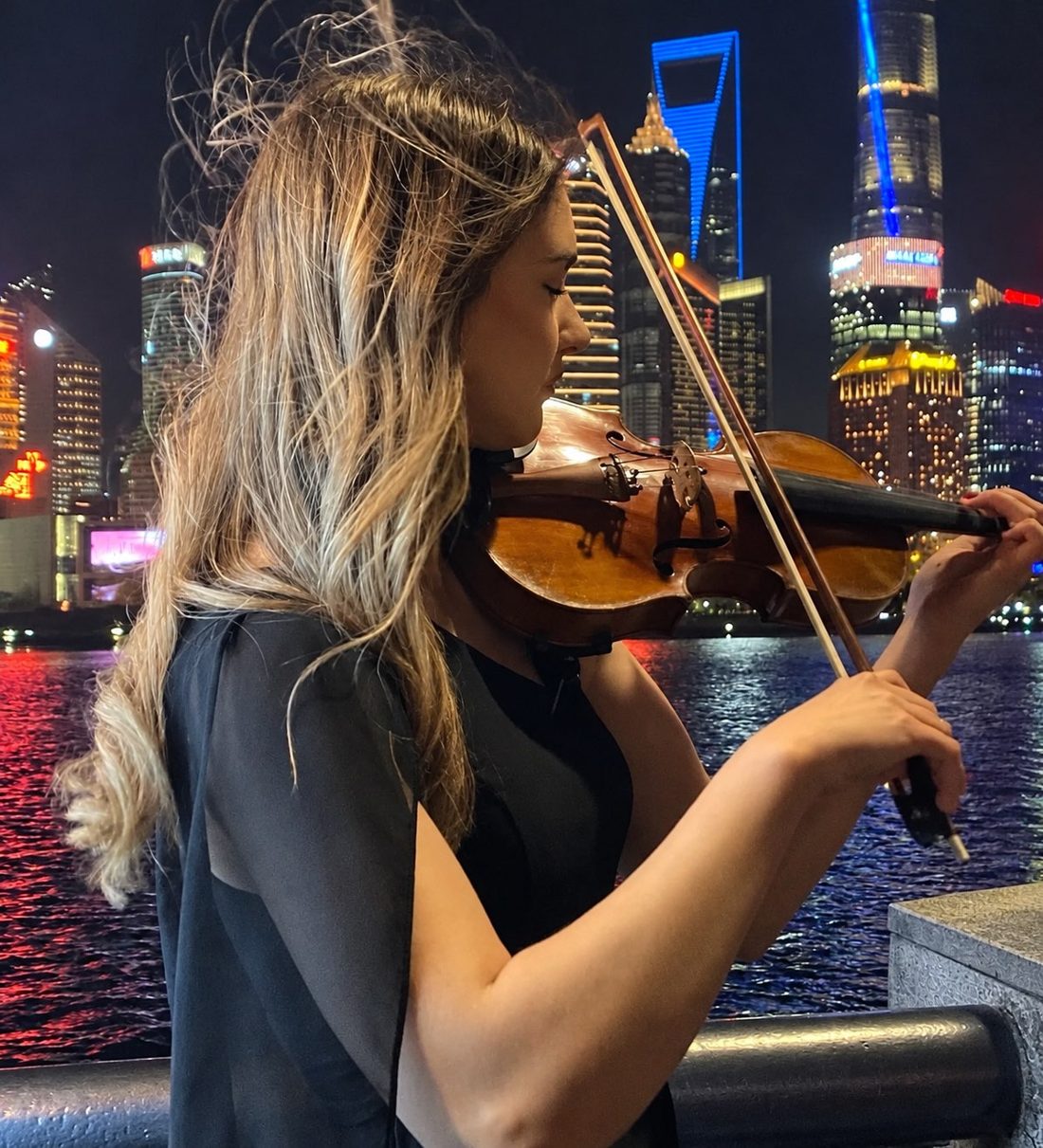 Anna-Emilia spielt Violine am Abend vor einer beleuchteten Skyline